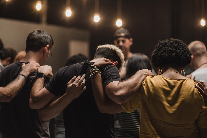 Personen stehen umarmend im Kreis und beten füreinander.